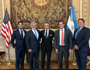 A group of five men, including Micucci and Nyce, pose for a picture in front of an earth-colored tapestry with the U.S. and Argentine flags.